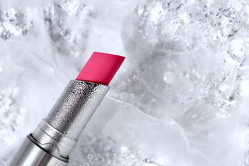 Pink red lipstick in silver tube on ice background, copy space
