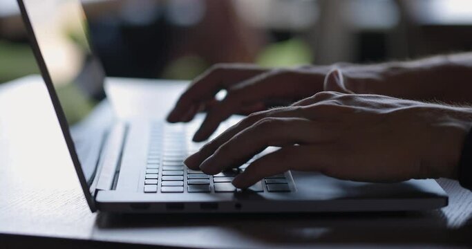 Close up of man's hands typing on laptop keyboard while sitting at table
