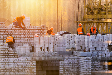 Bricklayer group workers installing brick masonry on exterior wall. Professional construction worker laying bricks. construction site at sunset