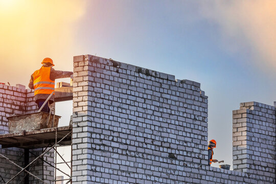 Professional construction worker laying bricks. Bricklayer workers installing brick masonry on exterior wall.