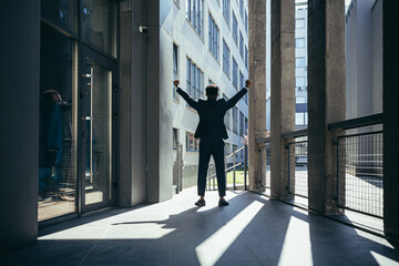 Fototapeta na wymiar Successful african american businessman with arms up celebrating victory. Concept: success, career growth, victory, freedom. silhouette business man on the background a modern office building. outside