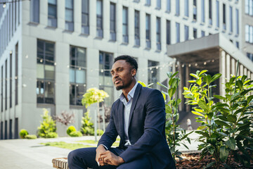 african american business man smoking cannabis outdoors sitting on city park bench on urban street background. Male employee Businessman. Office worker in suit Relieves stress a marijuana outside