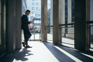 Fototapeta na wymiar Male businessman near office reads news from tablet computer, african american freelancer in business suit near office outside