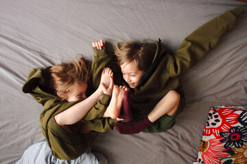 Two little friends, girls having fun at a pijama party at home, playing around on the bed