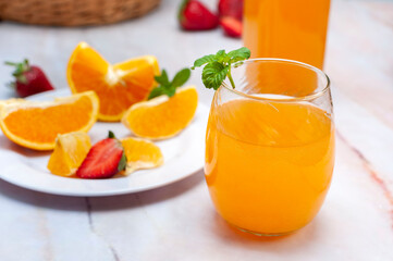 fruit juice and natural orange in glass and bottle with fresh oranges and strawberries on marble counter and white wall