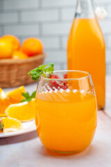 fruit juice and natural orange in glass and bottle with fresh oranges and strawberries on marble counter and white wall