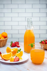 fruit juice and natural orange in glass and bottle with fresh oranges and strawberries on marble counter and white wall