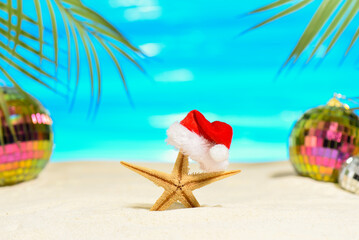 Fototapeta na wymiar Tropical Merry Christmas concept. Starfishe in a Santa hat on the sandy seashore. Mirrored trending disco balls and palm branches in the background.