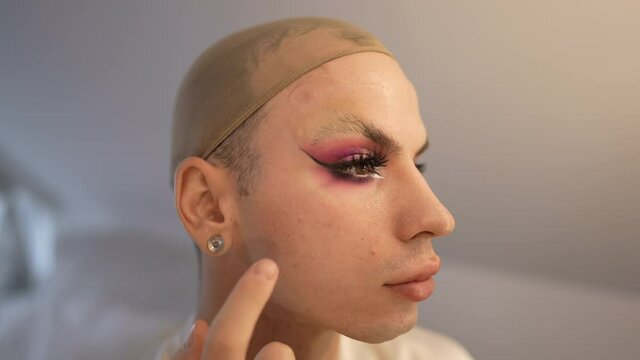 Side view face travesty woman applying false eyelashes in slow motion. Close-up portrait confident Caucasian queer LGBT person doing makeup. Identity and beauty