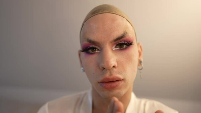 Close-up front view confident extravagant travesty woman adjusting false eyelashes looking at camera. Headshot portrait of Caucasian LGBT gender-fluid person with beautiful makeup posing indoors