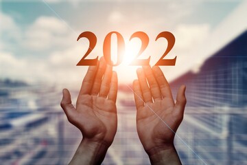 2022 is supported by hands on the background of a sunny sunset.