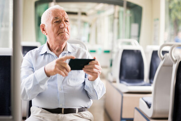 Old European man sitting in streetcar and using smartphone while waiting for next stop.
