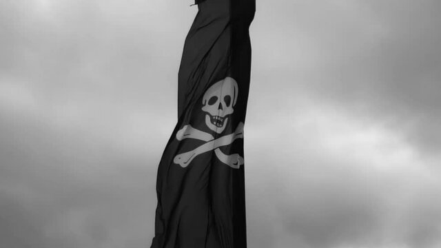 A pirate flag with a skull and bones waving on the cloudy sky