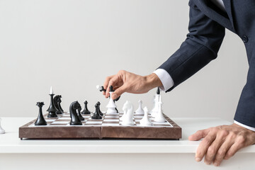 Young man playing chess on light background