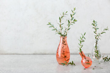 Stylish vases with green eucalyptus branches on table near light wall
