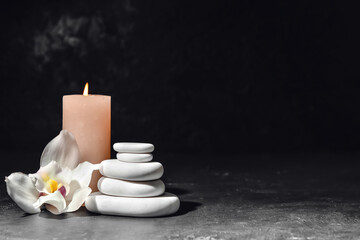 Stack of spa stones, flower and burning candle on dark background