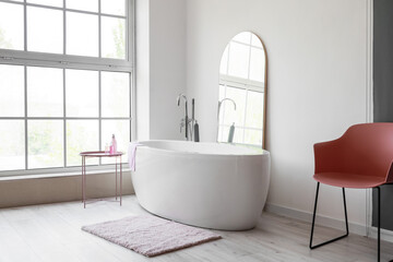 Modern bathtub and mirror in room with big window
