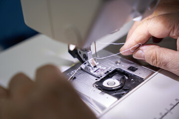 The workplace of a seamstress. The dressmaker works on a sewing machine. A tailor threads a thread into a sewing machine at his workplace. Hobby-sewing as a small business concept. High quality photo