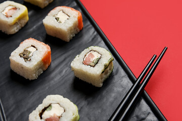 Tray with delicious sushi rolls and chopsticks on color background, closeup