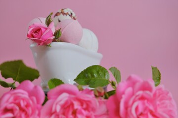 Bath bombs with rose extract in a bath and pink roses on a pink background.Pink bath bombs and pink...