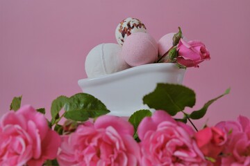 Bath bombs with rose extract in a ceramic bath and pink roses on a pink background.Pink bath bombs and pink rose flowers- Flower Bath Bombs.Beauty and aromatherapy. Organic vegan eco cosmetics.