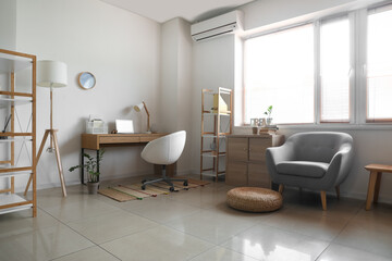 Interior of light room with modern workplace, floor lamp, shelf units and big window