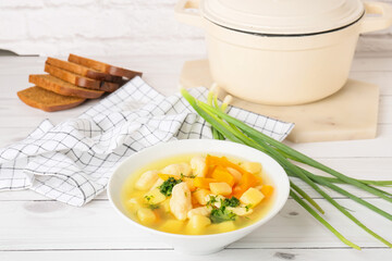 Bowl of tasty dumpling soup, bread and green onion on light wooden background