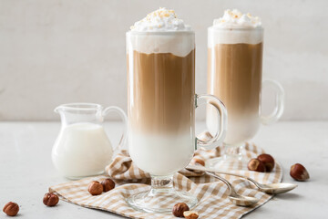 Glass cups of tasty latte with nuts on white background