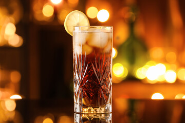 Glass of tasty Cuba Libre cocktail on table against blurred lights