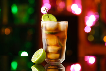 Glass of tasty Cuba Libre cocktail on table against blurred lights