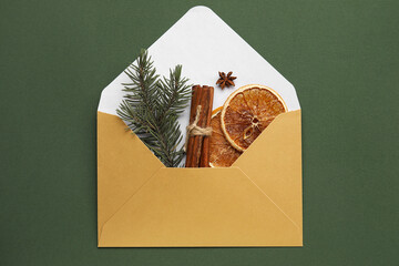 Envelope with fir tree branch, cinnamon, anise and slices of dried orange on green background