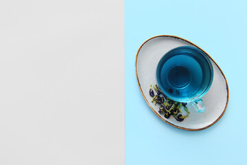 Glass cup of organic blue tea and dried flowers on color background