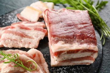 Board with uncooked bacon on black background