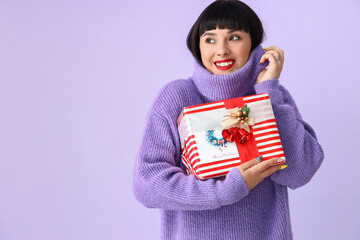 Beautiful young woman with Christmas gift on color background