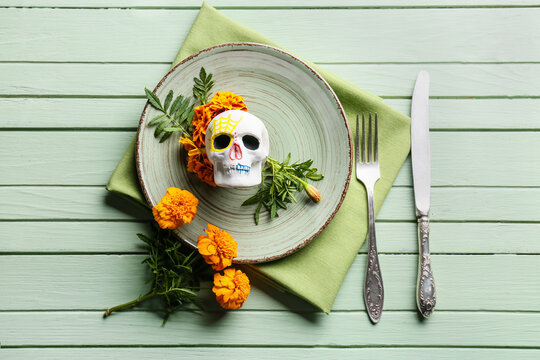 Table setting with human skull and flowers on green wooden background. Mexico's Day of the Dead (El Dia de Muertos)