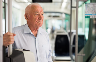 Naklejka na ściany i meble Senior European man standing inside tram and waiting for his stop.