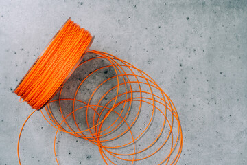 3d Printer Plastic Filament. Spool of orange  thermoplastic wire for 3D printing close up on grey stone background - obrazy, fototapety, plakaty