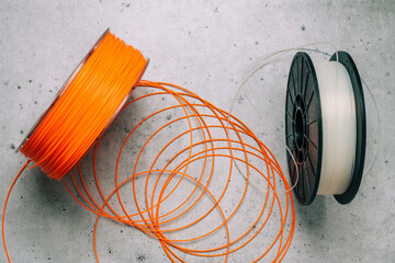 3D Printer Plastic Filaments. Spools of orange and white thermoplastic wires for 3D printing close up on grey stone background - obrazy, fototapety, plakaty