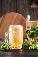 Glass of beer on wooden table with wheat ears and hop cones