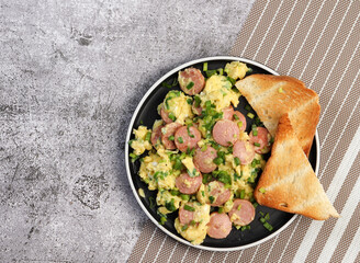 Scrambled Eggs with sausage and toast on a round plate on a dark background. Top view, flat lay