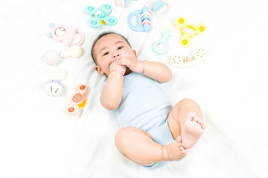 childhood and Childcare concept Portrait of cute little 5 months old asian newborn baby boy having teeth growing issues teething pain while holding a bite toy lying on the bed top view