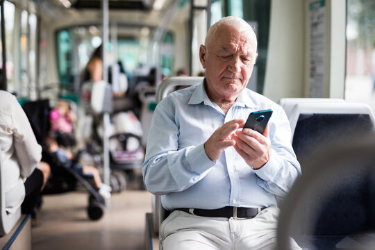 Old European man sitting in streetcar and using smartphone while waiting for next stop.
