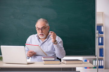 Old male teacher in front of green board