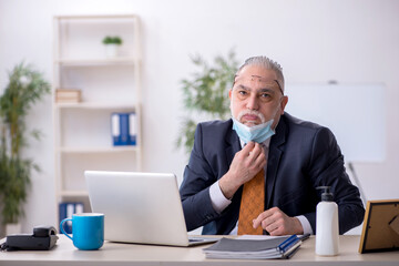 Old male employee working in the office during pandemic