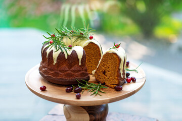 Christmas caramel cake, cutaway, decorated with white chocolate, cranberries and rosemary on a wooden stand. Festive baked goods. Soft selective focus. Horizontal, close-up.