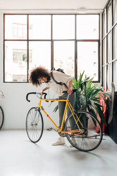 Young multiracial woman checking bicycle before leaving her apartment to go to college.Vertical image.