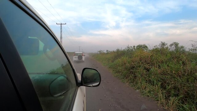 Three white vehicles drive in convoy on lowland dirt road in Africa