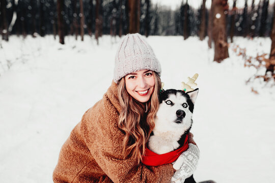 Portrait photo of girl and dog on white snow in winter forest at Christmas