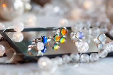 Multi-colored rings made of dichroic glass using the fusing technique lie on a mirror-like surface, handmade