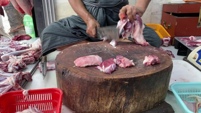 Butcher cutting raw meat in India with big knife. He is making pieces for keema, kabab, nalli, paya muslim dishes.